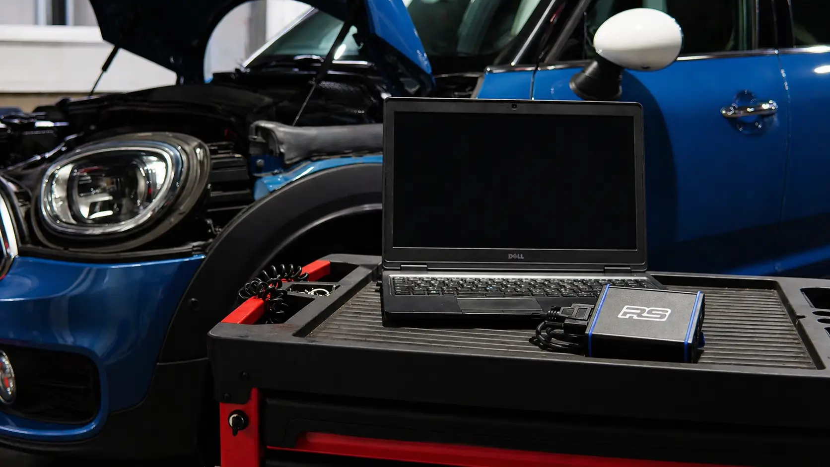 Ordinateur de diagnostic posé devant le moteur d’une voiture, capot ouvert