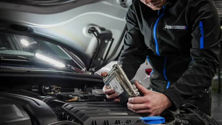 Technicien RS Tronic tenant un calculateur moteur au-dessus du compartiment moteur